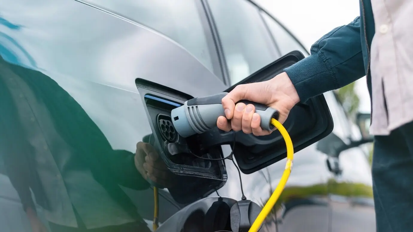 A man connecting a charger to an electric car at a charging station.