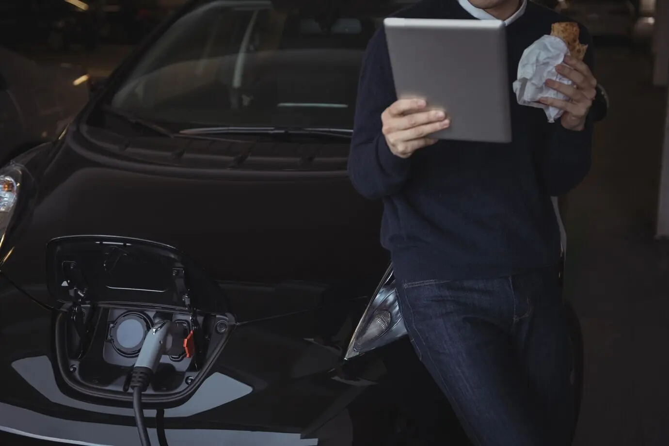 A man uses a digital tablet as he charges an electric car.
